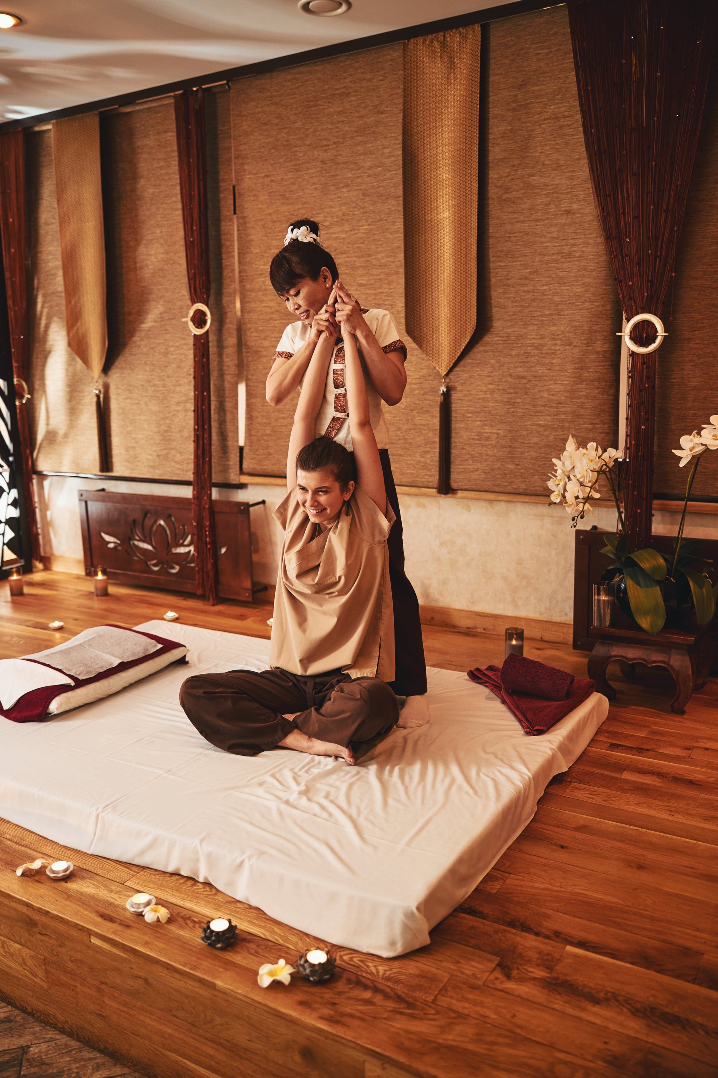 A stretch — the therapist stands behind the seated guest and lifts the arms overhead