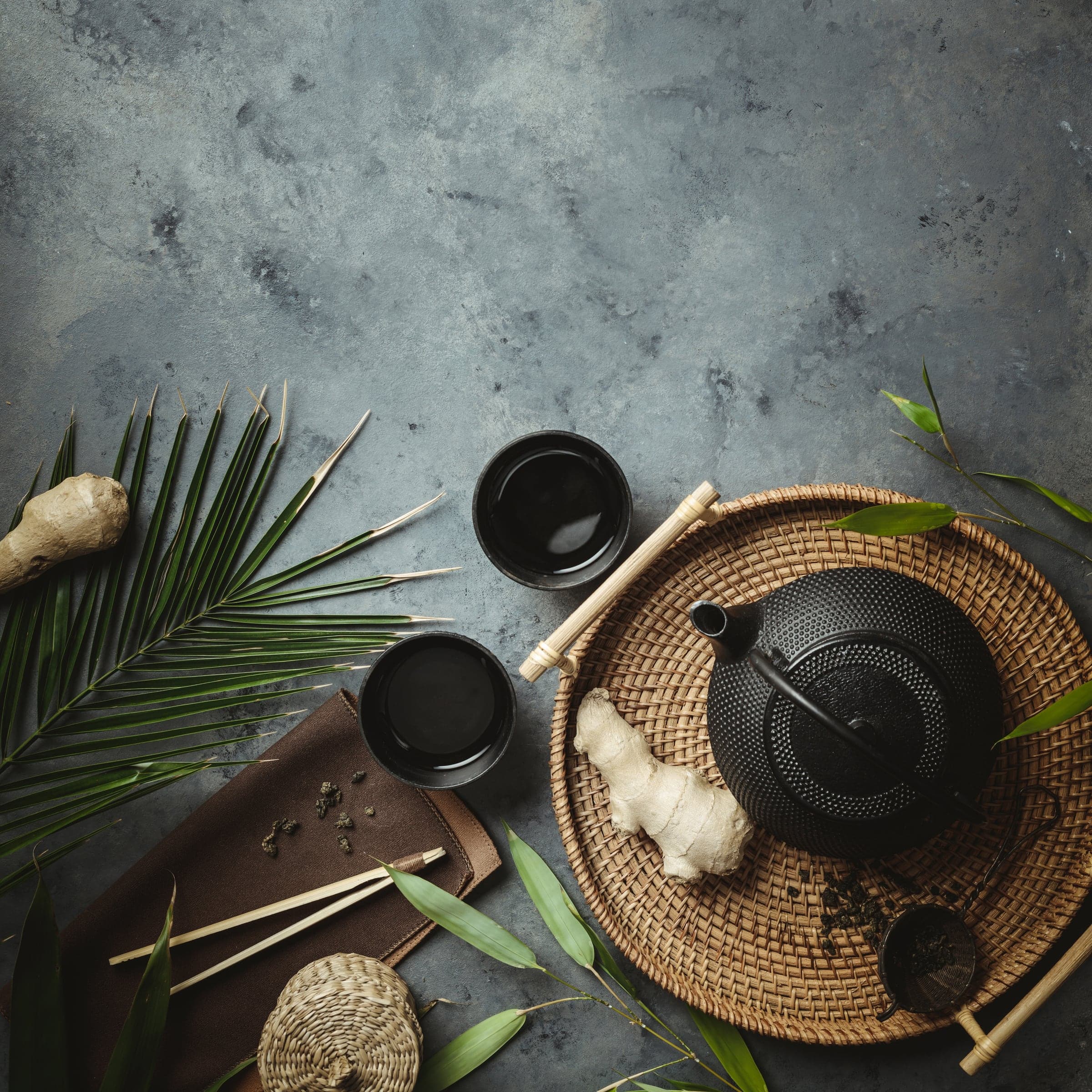 Tea after the treatment — a black iron teapot, cups, ginger and a palm leaf on a woven tray