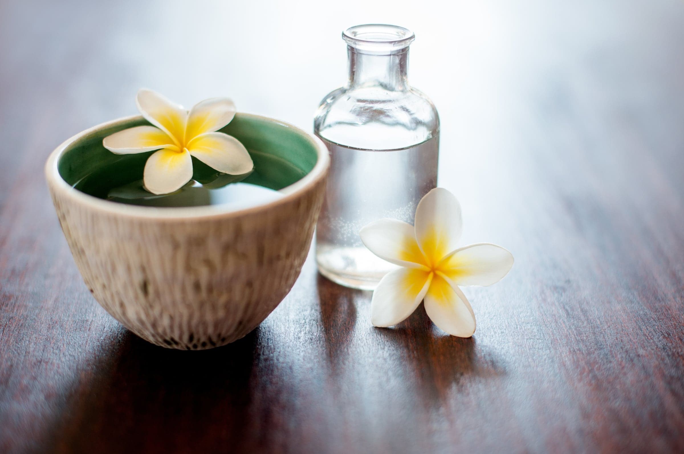 Plumeria flowers in a bowl of water on dark wood