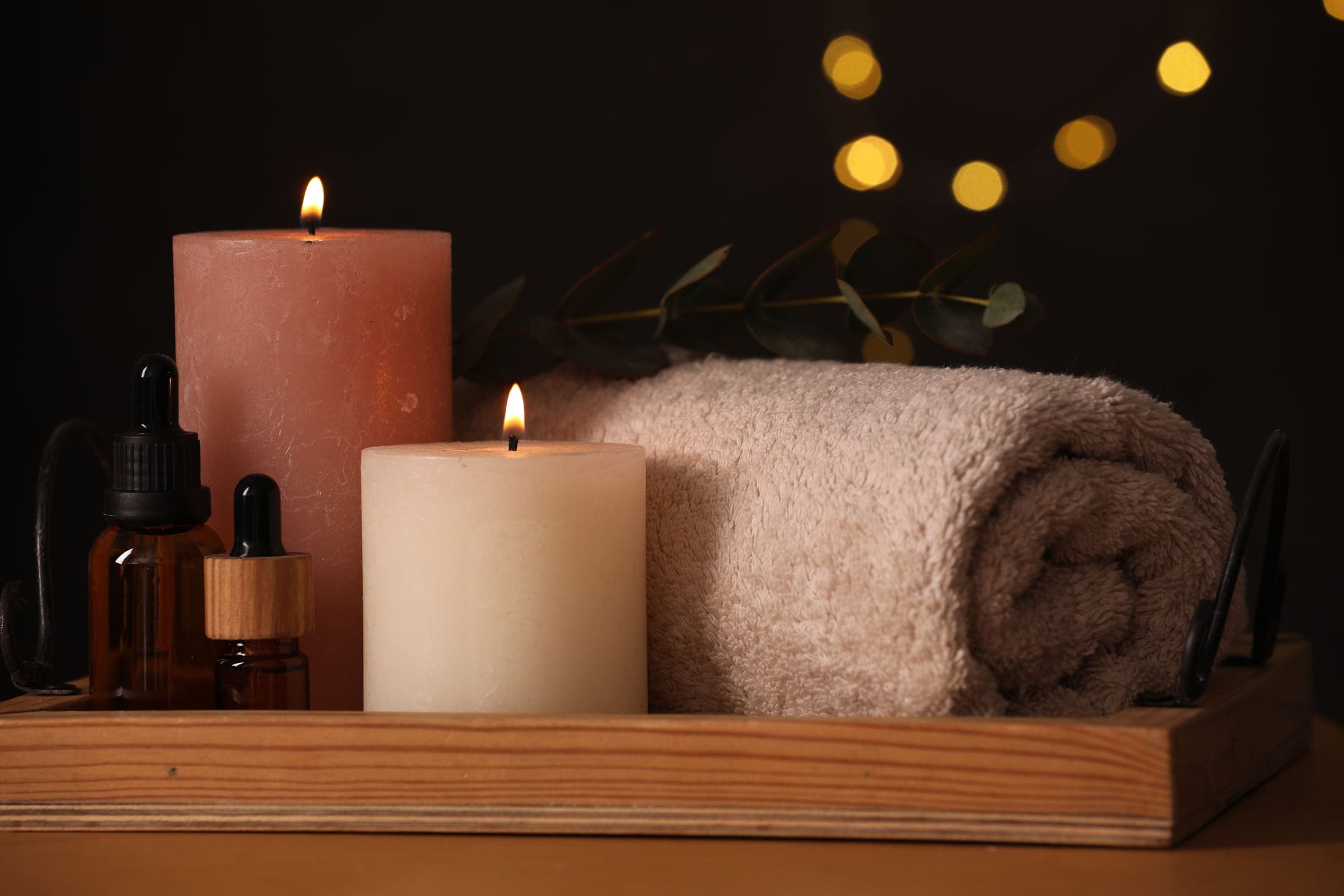 A gift from the house — candles, massage oils and rolled towels on a wooden tray in warm light