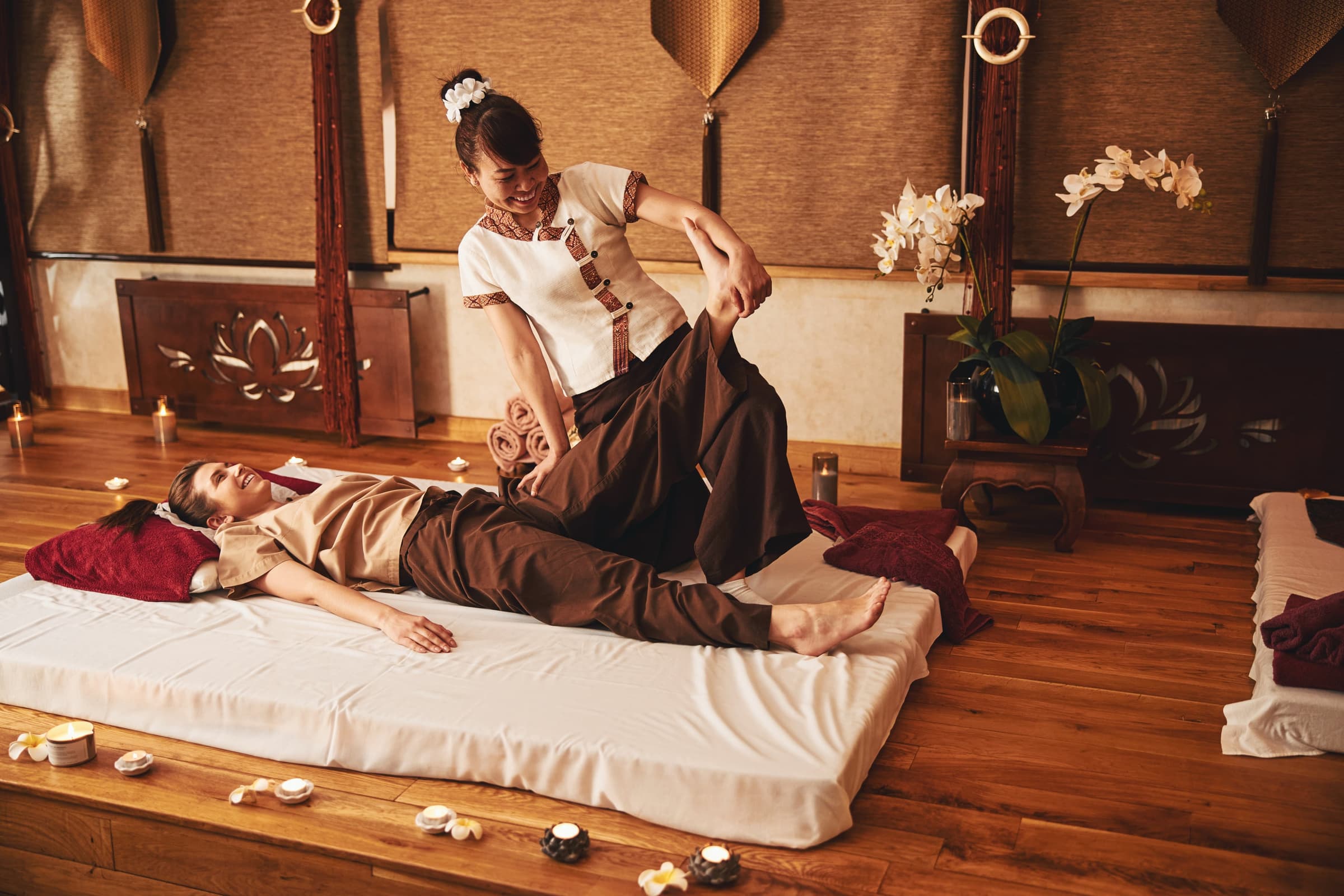 The house — a therapist kneels by a guest lying on a mat in a warm room, candles and orchids around