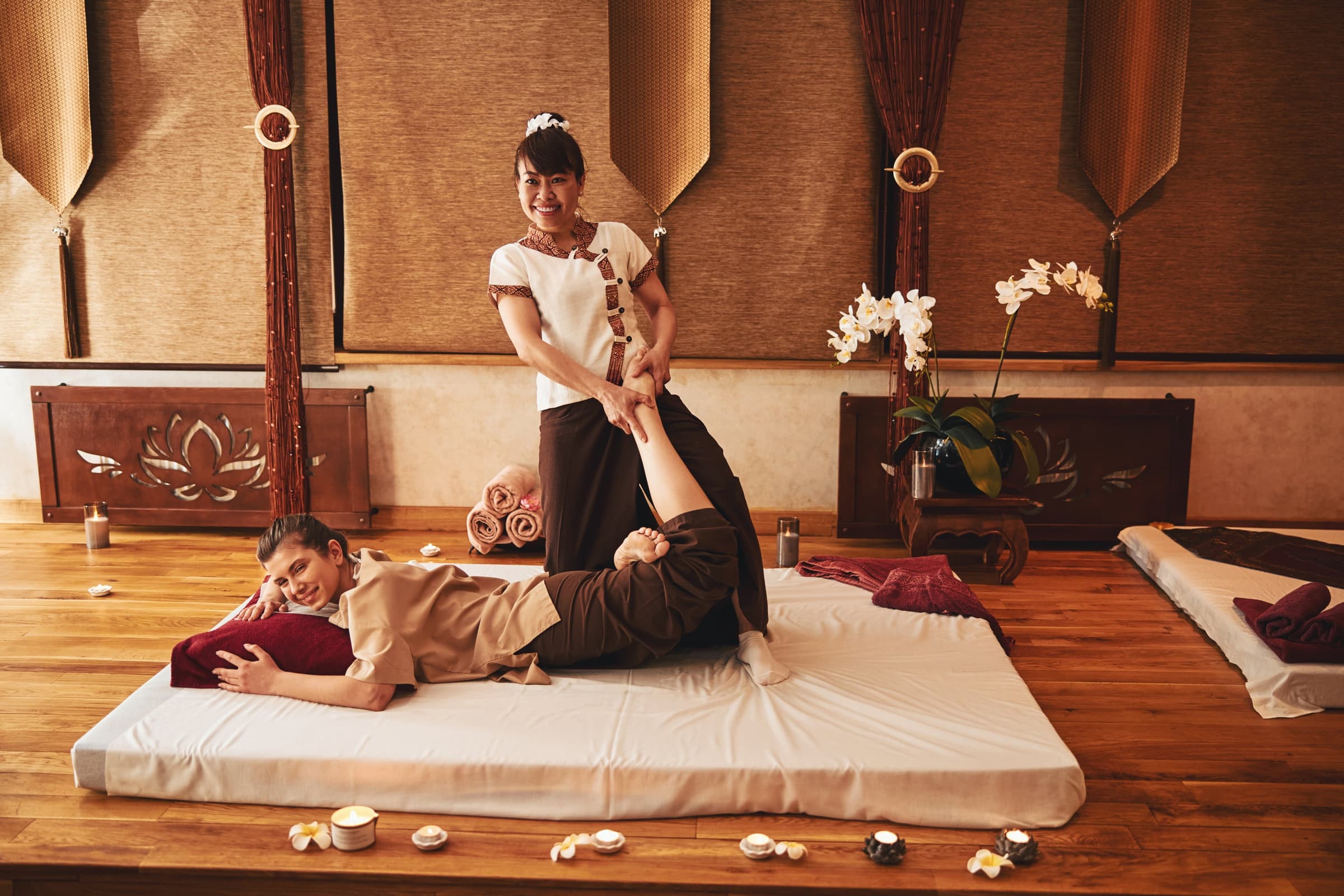 Traditional Thai massage — a leg stretch on the mat in a teak-lined room